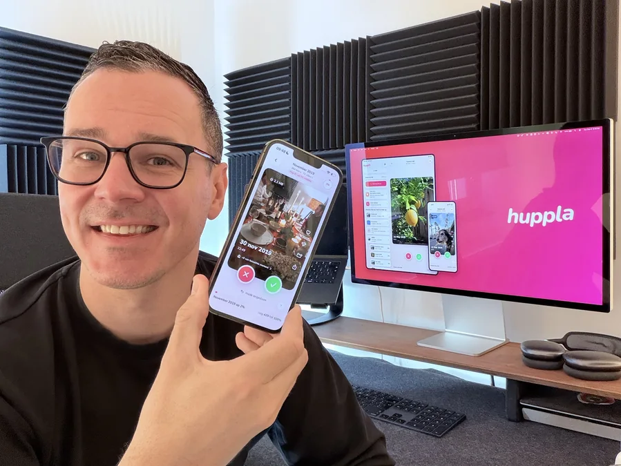 Matthi holding an iPhone running Huppla, a large screen behind him showing the app on iPad and iPhone